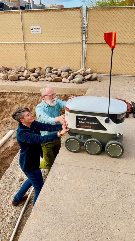 Me: a late 30s white lady with short hair and a killer dark teal blazer. 

Him: my former professor who looks exactly like what you would expect - a 60 something tall pale white dude with white hair and a large white beard. 

The scene: Downward looking angle showing us standing in a stepped very large hole in a construction area. We have just hoisted one of those food delivery robots (a cooler on six wheels with a lil flag) back onto the concrete at ground level. 