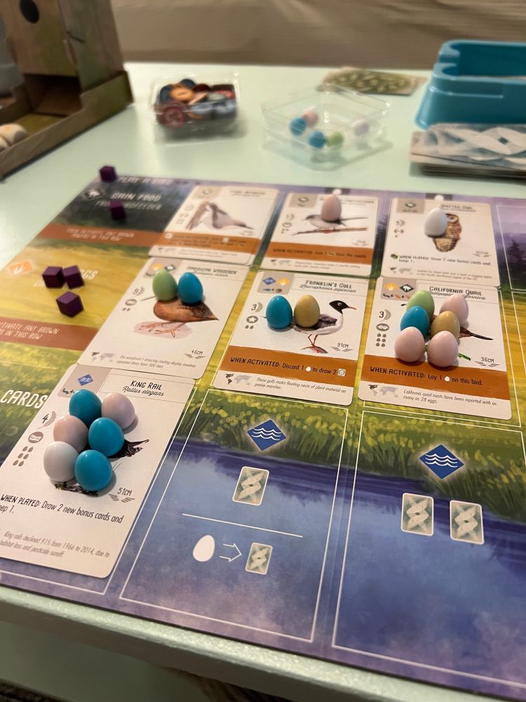 Photo of a wingspan game board with many eggs on several birds.