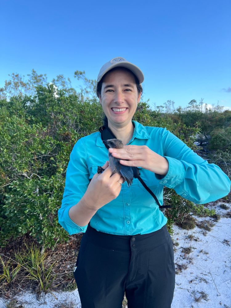 Photo of a smiling Angela carefully holding a young Florida Scrub-Jay (with no visible tail feathers).