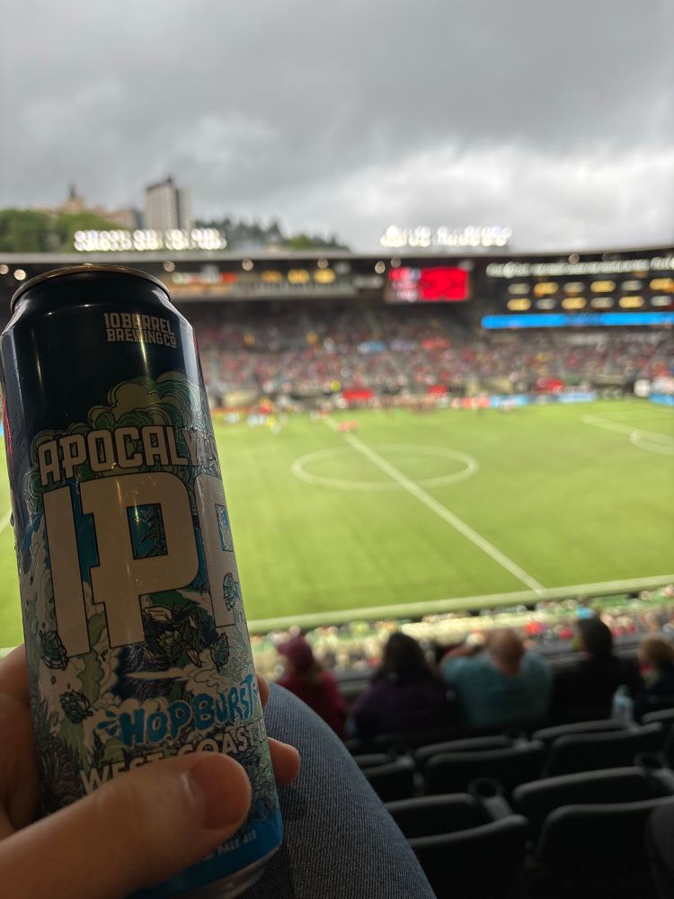 Holding a can of Apocalypse IPA in foreground, Providence Park field in background 
