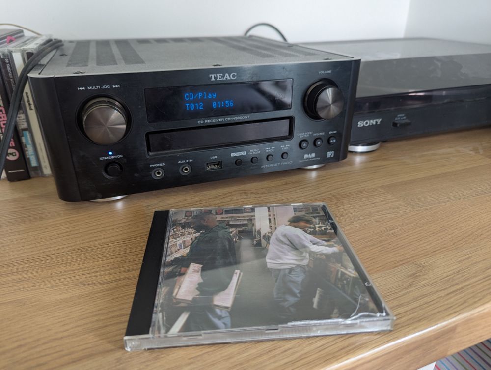 Photo of a CD player, with a CD case on a shelf in front of it. The CD is DJ Shadow - Endtroducing...