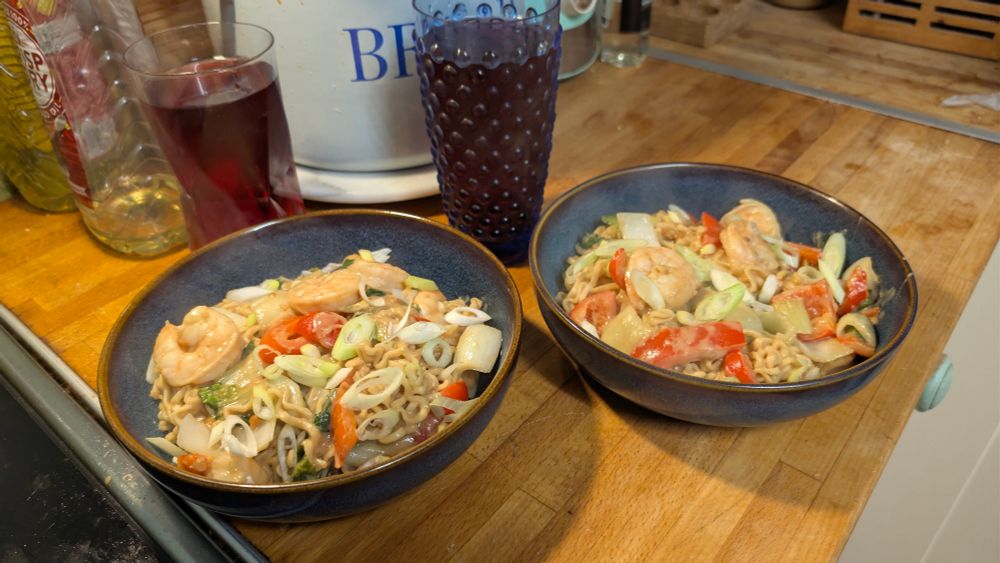 Two bowls of pad thai and two glasses of Vimto squash.