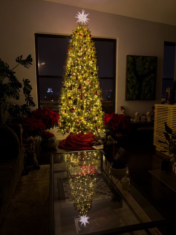 A bright Christmas tree in a darkened living room at night giving off a warm glow covered in ornaments. 