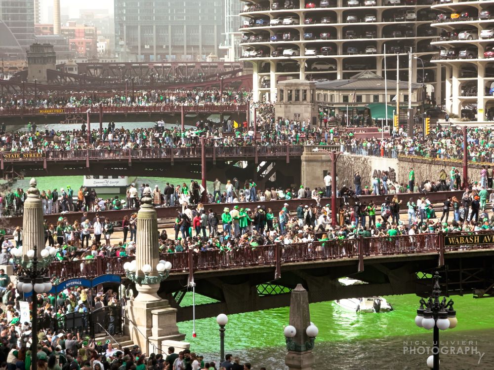 A shallow telephoto image of Chicago's famous bridges on St. Patrick's Day. The brides - stretch the entirety of the frame and are covered in with people looking at river's water dyed green in celebration of St. Patrick's Day
