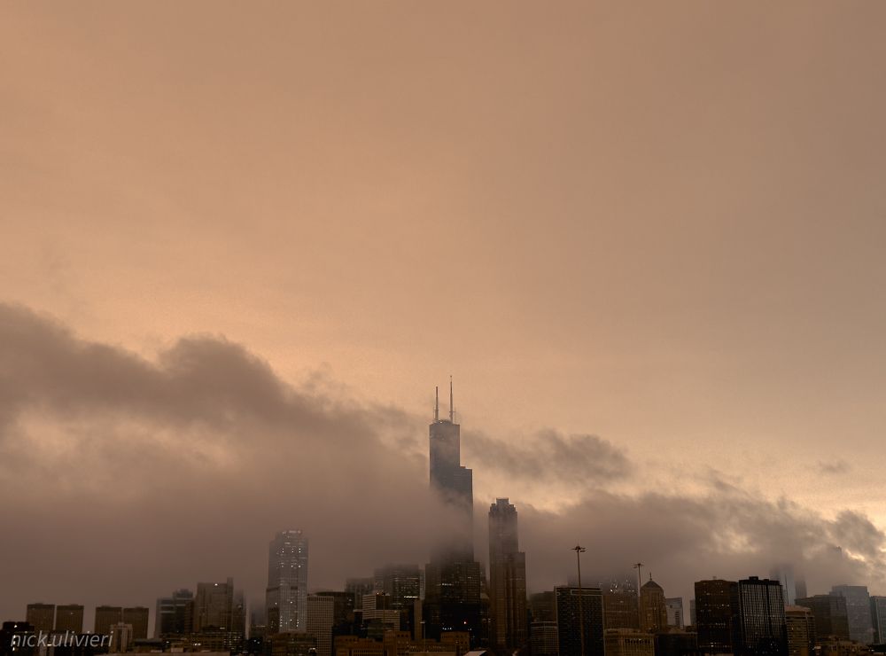 A view of the Chicago skyline during g a rainstorm. The sky is tinged brown/orange with dust from plains dust storm infiltrating the clouds