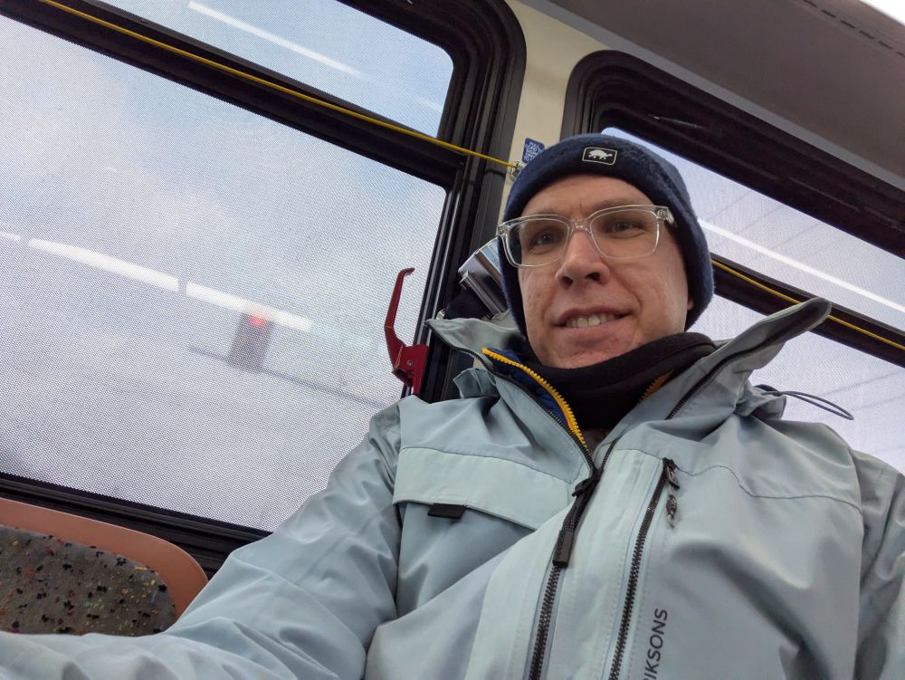 Picture of me sitting inside a CATA bus with a blue jacket and hat and bus windows behind me.