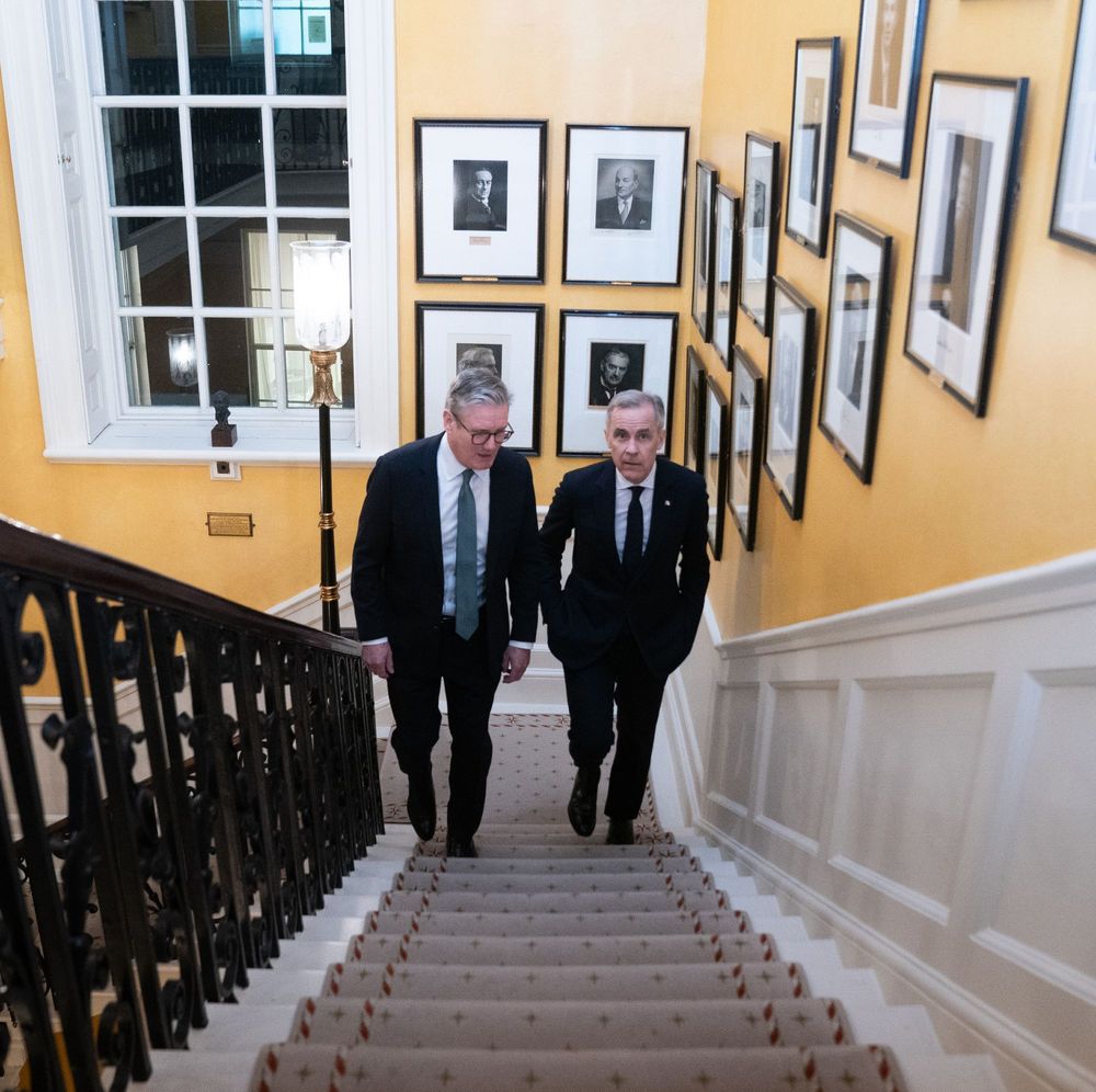 Prime Minister Keir Starmer and Prime Minister Mark Carney walk up a set of stairs inside 10 Downing Street. 
