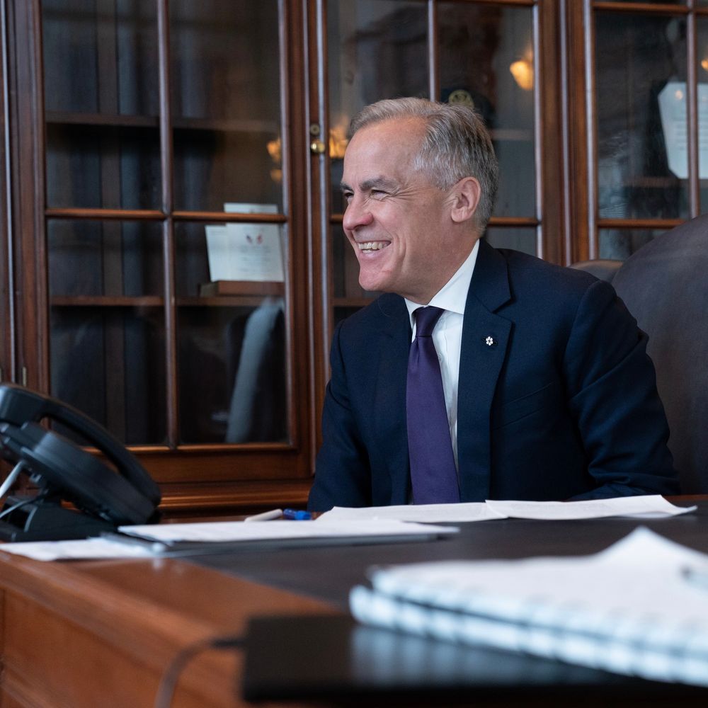 Prime Minister Mark Carney smiles while on the phone with President Sheinbaum, sitting behind his desk in his office in Ottawa, Ontario.