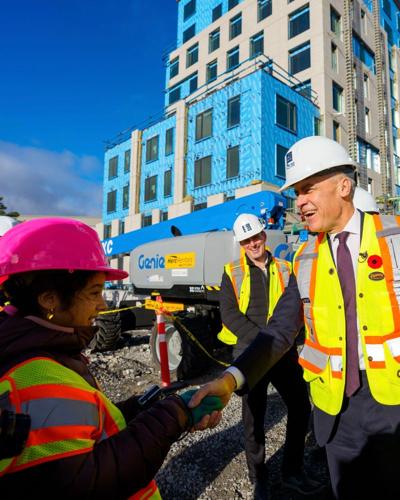 Prime Minister Carney shakes the hand of a youth wearing personal protective equipment at a construction site.