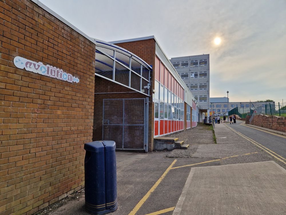 A photo of the old school stretching into the background with the new school behind it. The word evolution is written on the wall.