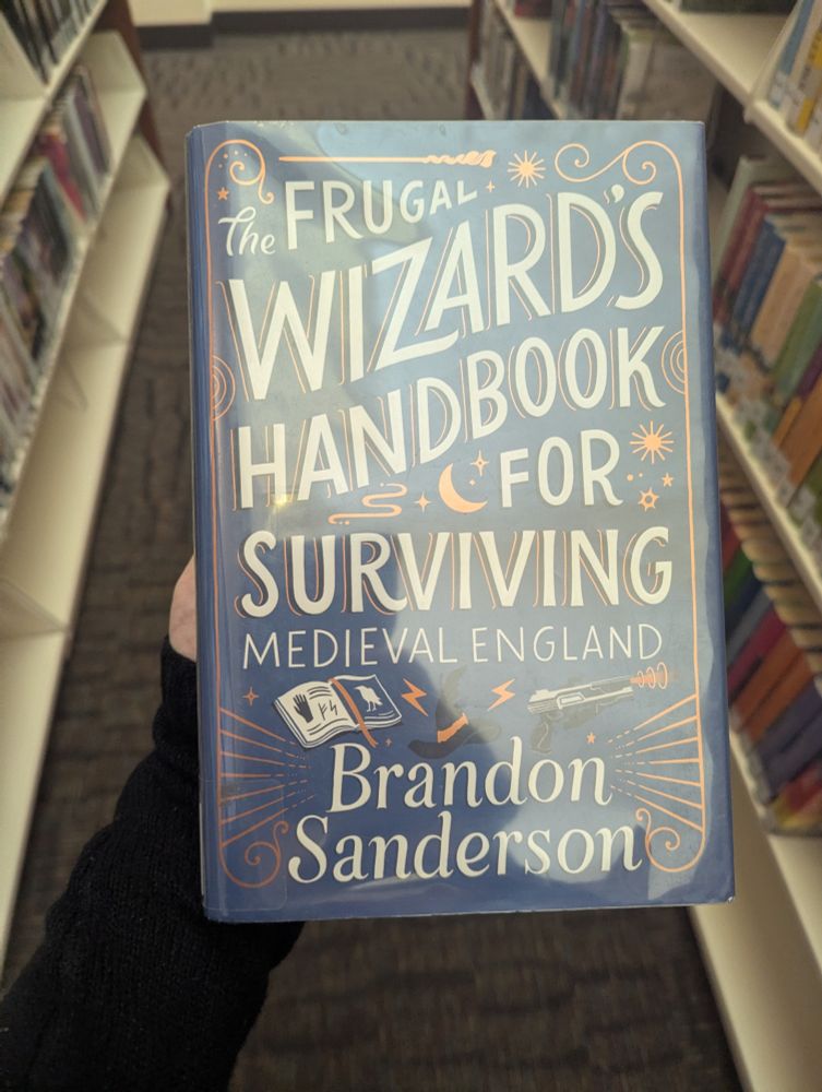Picture of The Frugal Wizard's Handbook for Surviving Medieval England by Brandon Sanderson taken between the book stacks in the library 
