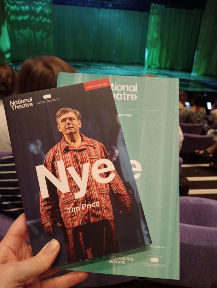 Nye play text and programme being held up with the stage in the background.
