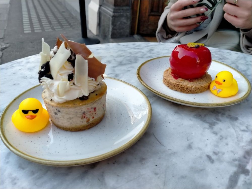 A beige cake on the left, with a little rubber duck with sunglasses to the side, and a red apple-shaped cake on the right, with a little rubber duck with a bow tie.