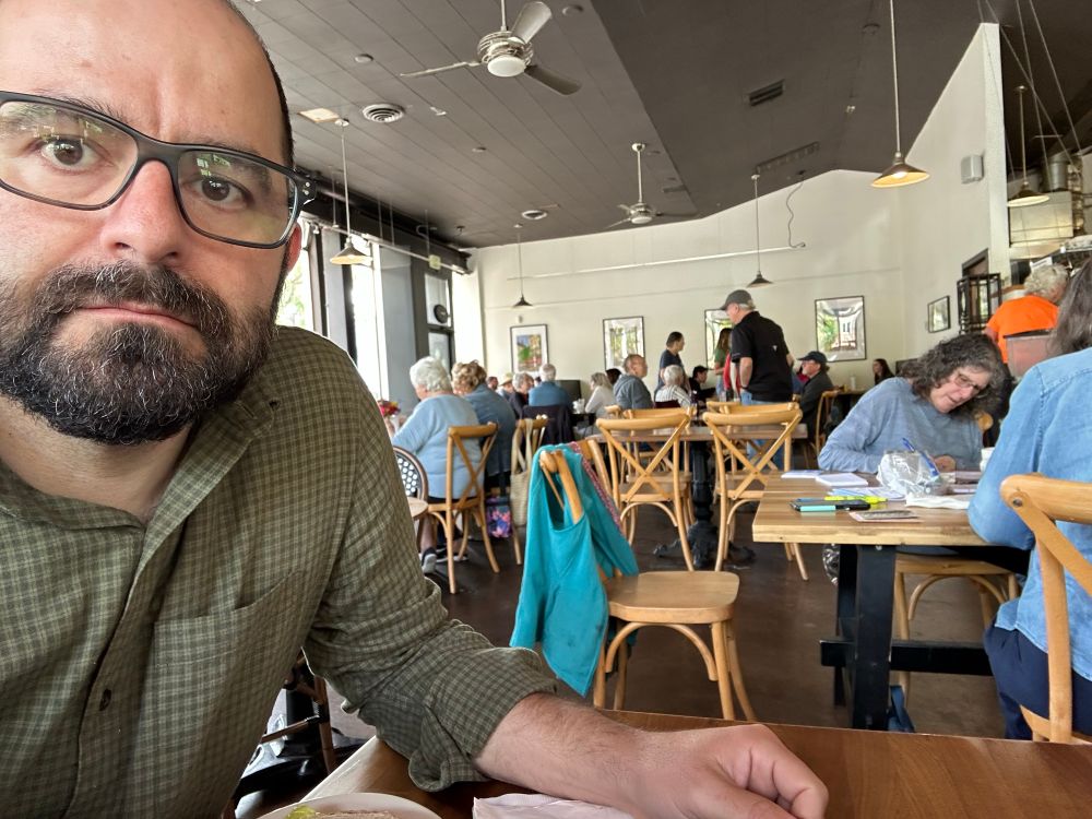 Selfie of the author with crowded tables of diners behind in a bakery/cafe