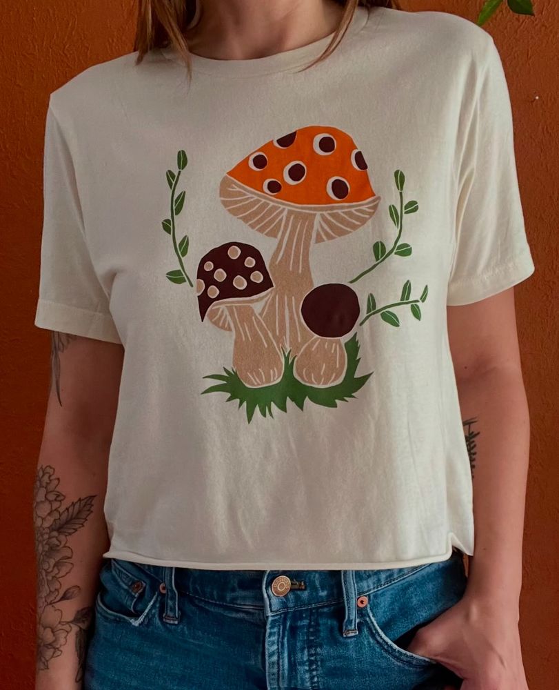 Woman wearing a white crop top with screenprinted orange and brown mushrooms.
