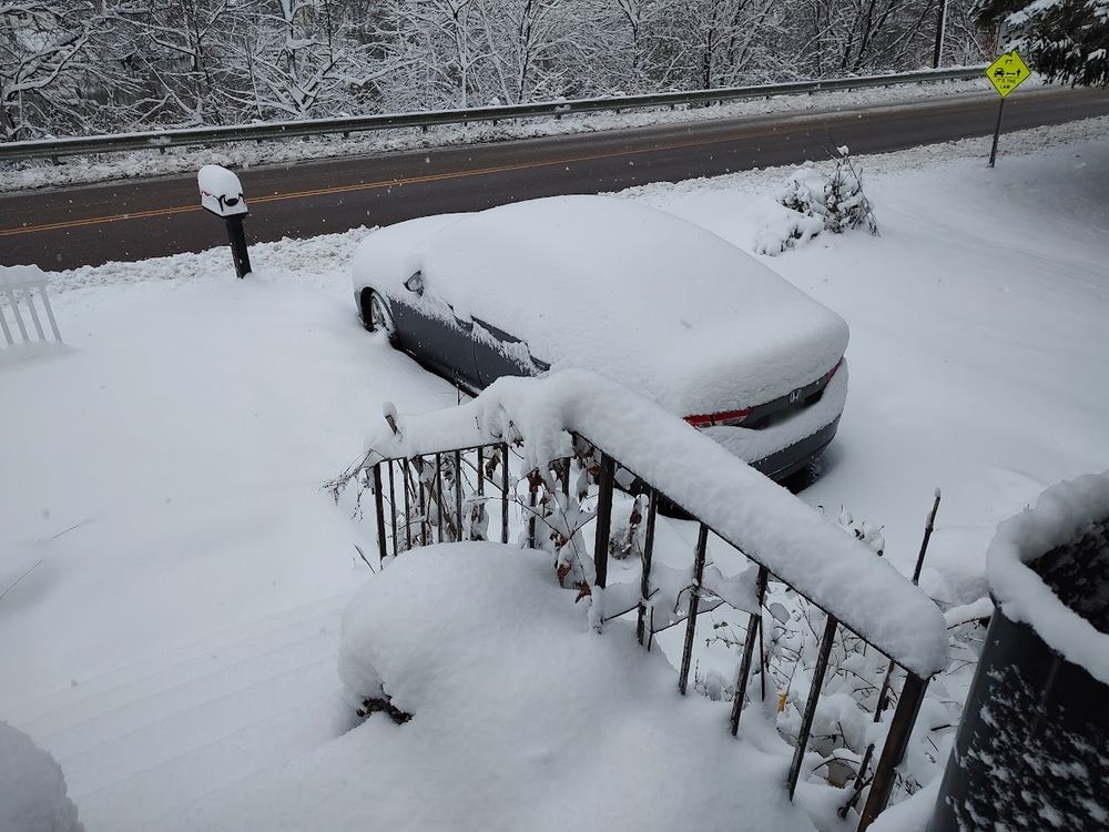 a photo of front porch stairs, part of a yard and a car in a driveway, under many inches of snow