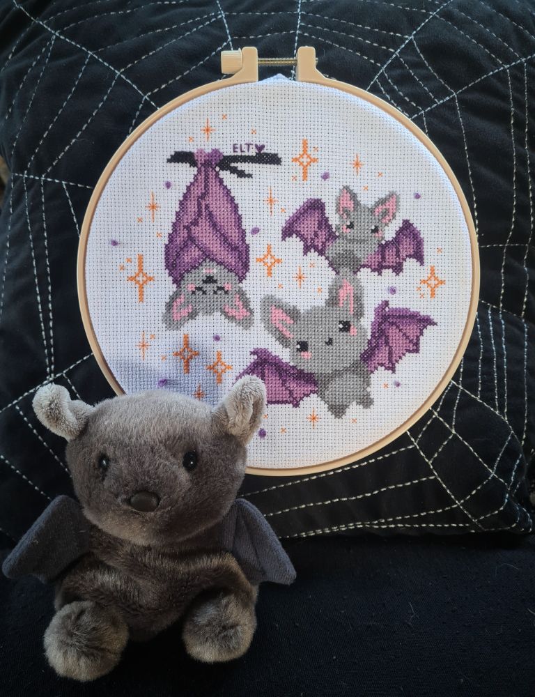 The same cross stitch hoop featuring a small hand sized plush bat sitting in front 
