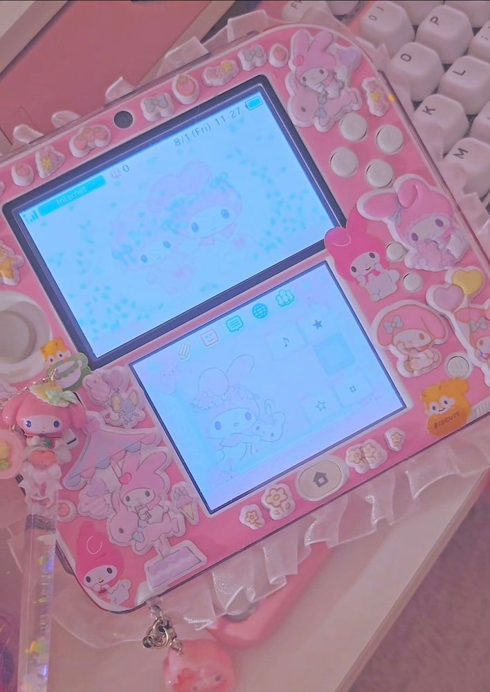 A pink nintendo 2ds decorated with my melody stickers and a frilly ruffle lace around the edges.