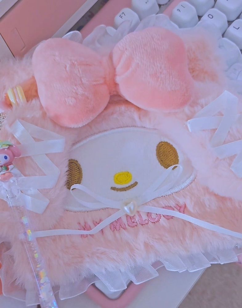 A pink nintendo 2ds decorated with a fluffy and frilly ruffle lace my melody themed case on the back with a sparkly my melody stylus next to the device.