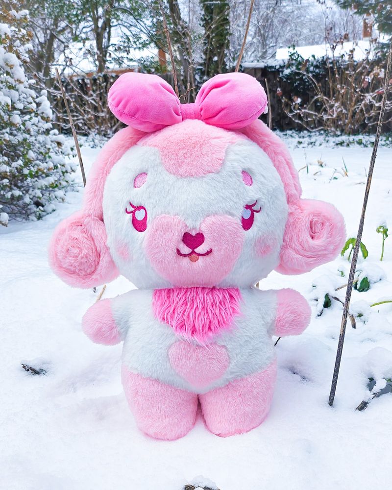 A stylized bipedal mostly white and pink dog character plush standing in the snow