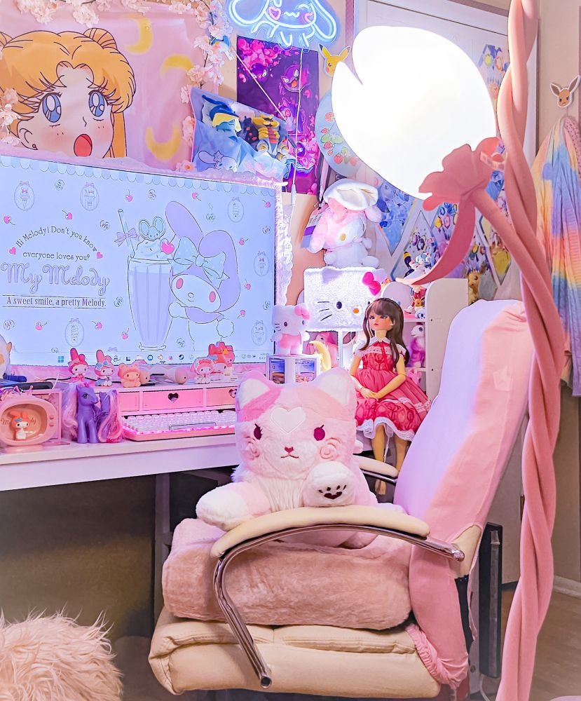A very pink themed cutesy gaming set up with a pink and white large cat plush sitting on the chair.