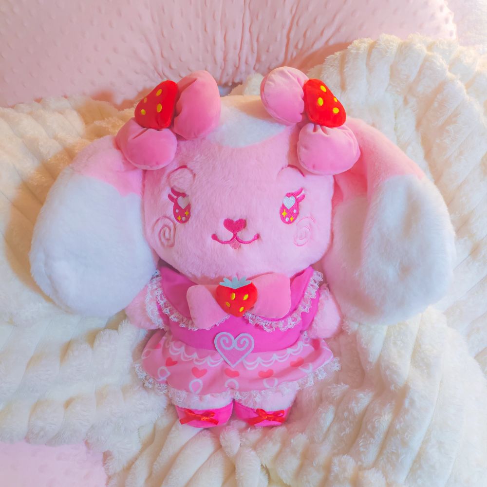 A stylized bipedal mostly light pink and white lop bunny character plushie with an ornate strawberry themed magical pink dress.