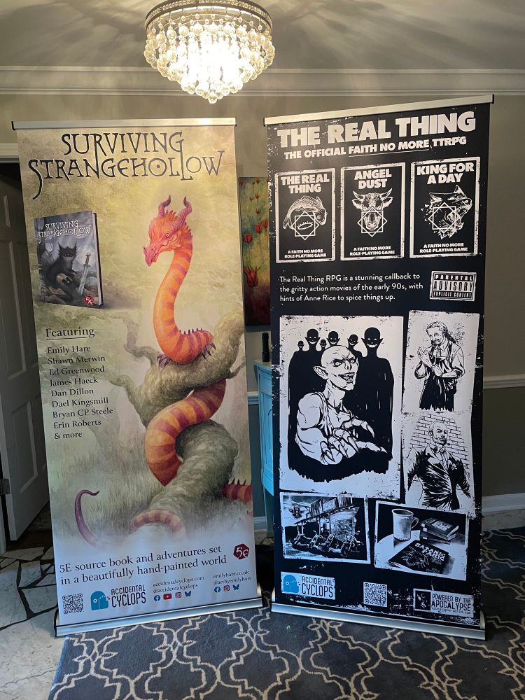 Photo of two standing banners. One of Surviving Strangehollow and one of The Real Thing RPG.