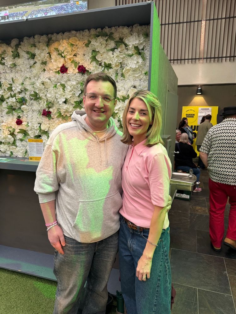 Niall in a grey hoodie and blue jeans hugging Grace Helbig in a pink polo and even bluer jeans