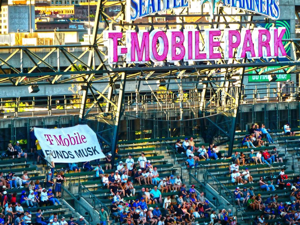 Banner reading “T-Mobile Funds Musk” being held inside T-Mobile Stadium at a Mariners game