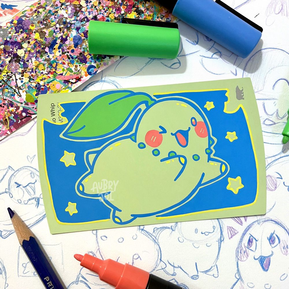 A cute, stylized paint pen illustration of Chikorita on a soft green paint swatch card. The color of the card is used as Chikorita’s base, so he’s heavily just illustrated with outlines. The painting sits on top of a sketchbook page filled with Chikorita sketches.