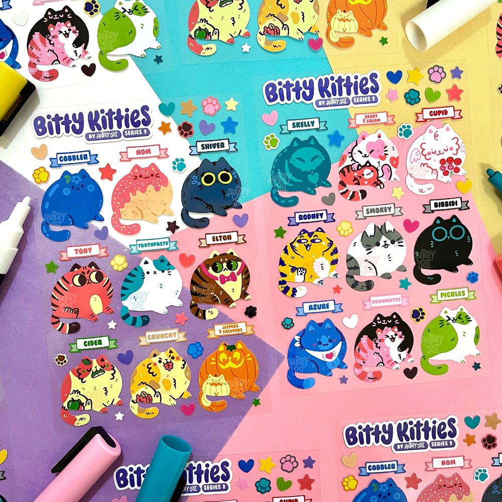 A photo of two sticker sheets with clear acetate backing. Each sheet has the Bitty Kitties logo in the top left corner. Each sheet has 9 unique fat cat designs on it, and all 18 cats are different. The cats range from natural colors like gray & brown tabbies, black cats, & calicos, to themed ones like fruit, skeletons, pumpkins, to unnatural colors like green, blue, & pink. They each have a name tag sticker above them. Both sheets also have a handful of tiny star/pawprint/heart filler stickers.
