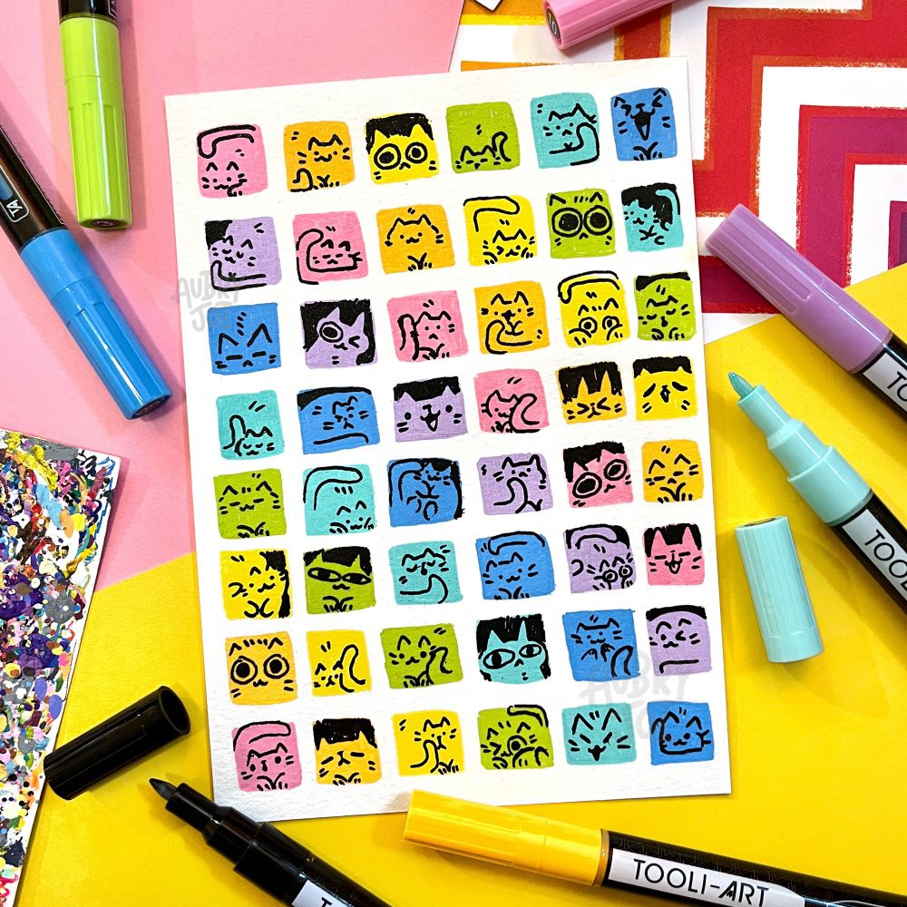 A grid of pastel rainbow cubes painted in a repeating pattern, filling a page. Each cube has a tiny cat illustrated into it, either a face or filling up the whole cube, in black. Several paint pens lay around the illustration.