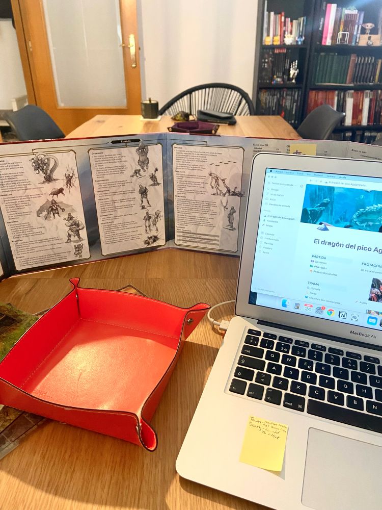 Foto de una mesa con una pantalla de máster, bandeja de dados y portátil con el Notion abierto.