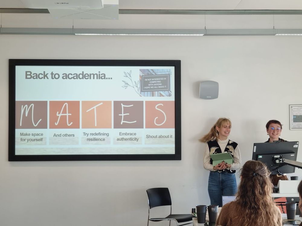 Two folks (Brodhie and Ron) happily presenting with a PowerPoint that reads, “MATES (make space for yourself, and others, try redefining resilience, embrace authenticity, shout about it)”.