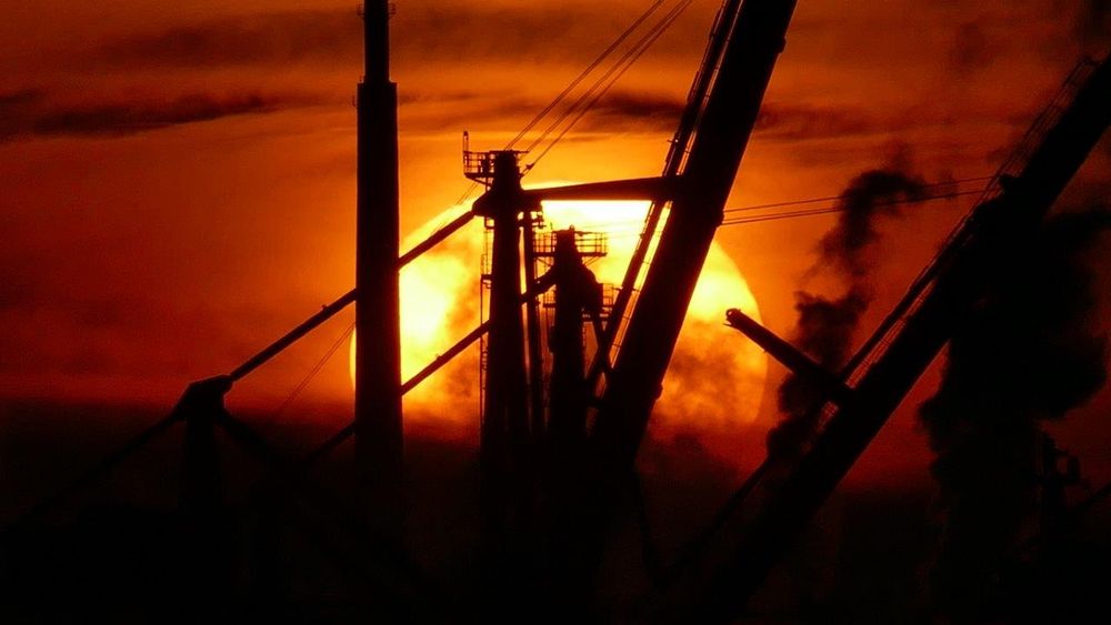 Silhouette eines Schiffes in Hamburg vor einem leuchtenden Sonnenuntergang mit Rauchwolken und strukturellen Kränen.