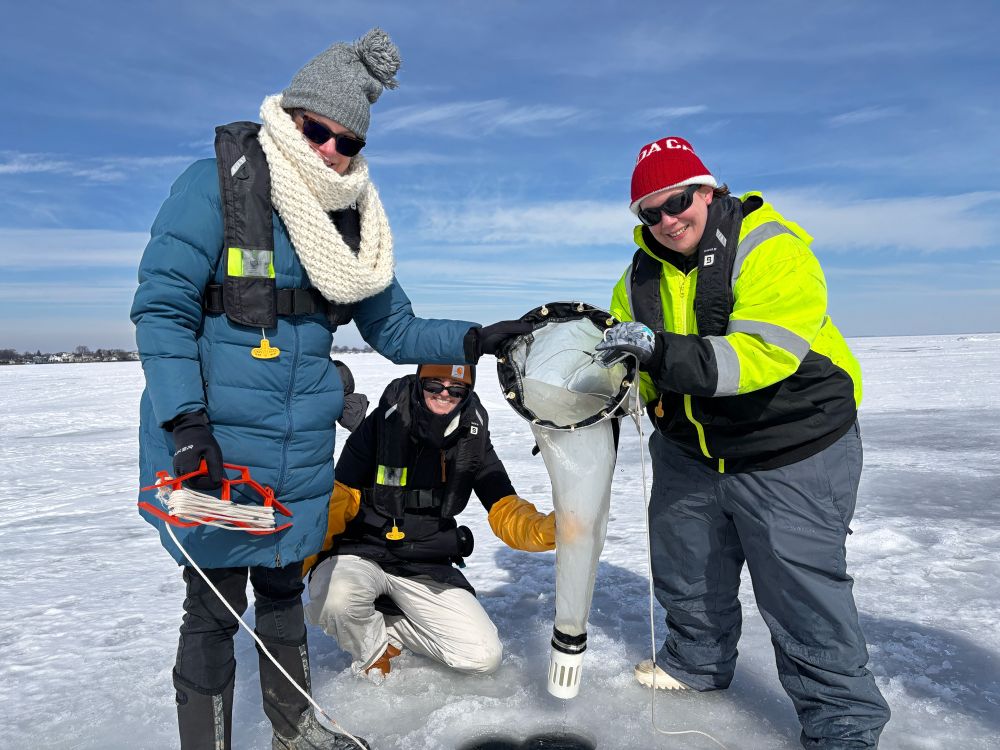 Three women scientists holding a zooplankton net over an ice hole