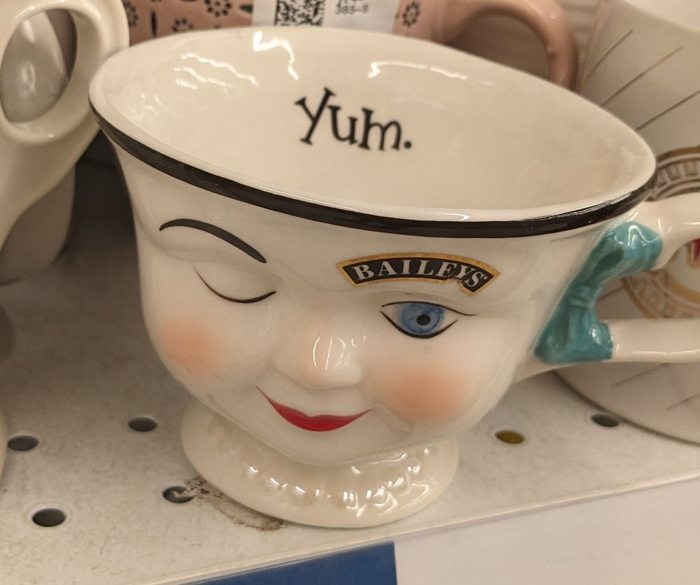 A Bailey's brand mug with a porcelain doll face winking at you with the inscription "Yum." on the inside lip of the mug.
