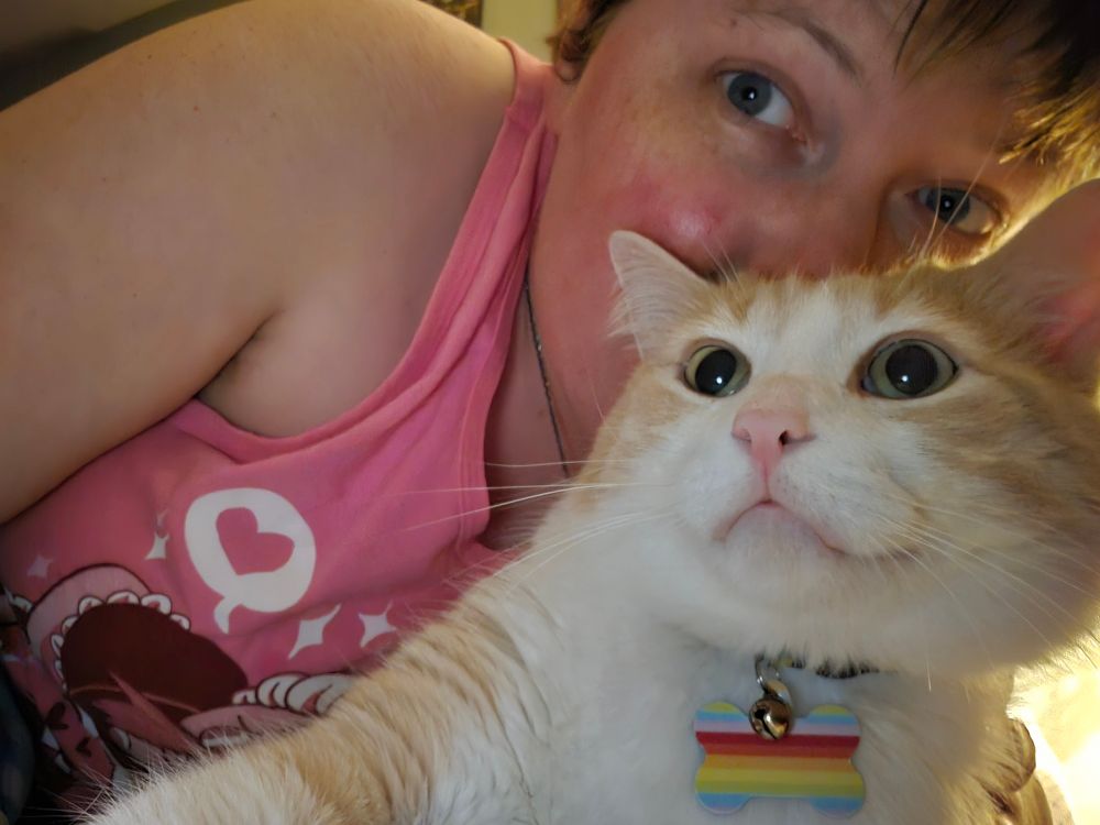 A photo of me leaning into Bubba, an orange and white cat. We're both looking to the left into the camera. I look happy and a bit inebriated, Bubba looks apprehensive