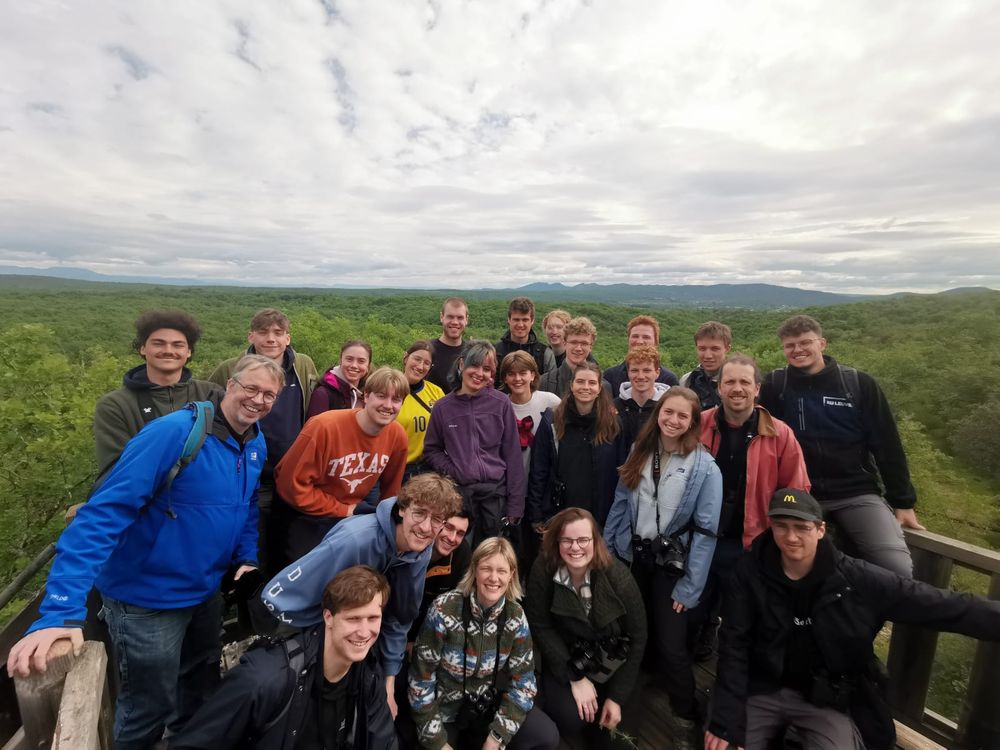 A group of people posing on a viewing platform. Behind them are rolling hills of green oak woodland.