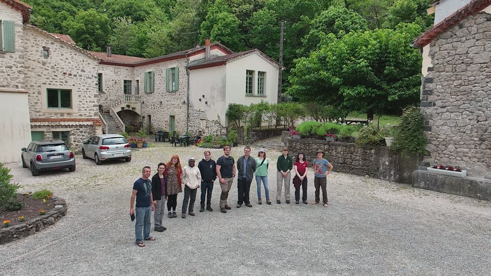 A photo of a group of people in front of a traditional Mediterranean building with a wooded hill in the background.