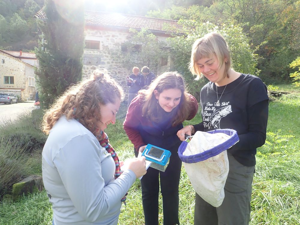 A group of students examining the contents of their sweep net for collecting insects. In the background more students are looking at a field guide to identify their findings. It is autumn and the sun is shining on the old buildings of the chateau behind them all.