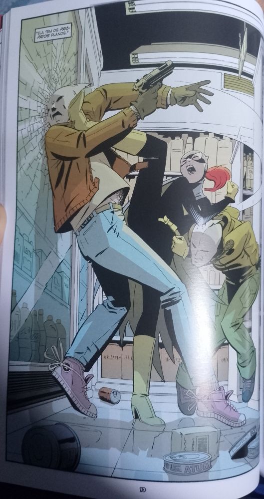 Página de Batgirl Ano Um. Batgirl (Barbara Gordon) metendo o cacete em dois assaltantes em um mercadinho. Na página, ela chuta a cara de um contra o vidro enquanto dá uma chave de braço no outro.