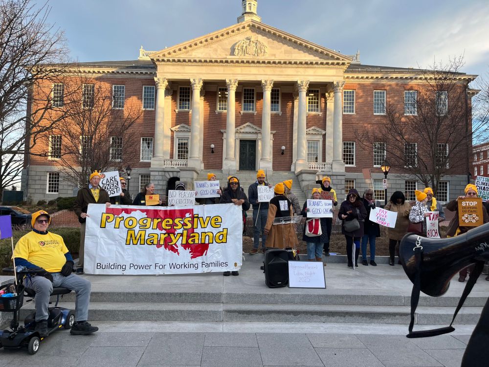 A crowd of people holding a Progressive Maryland banner stand in front of the Maryland State Capitol 