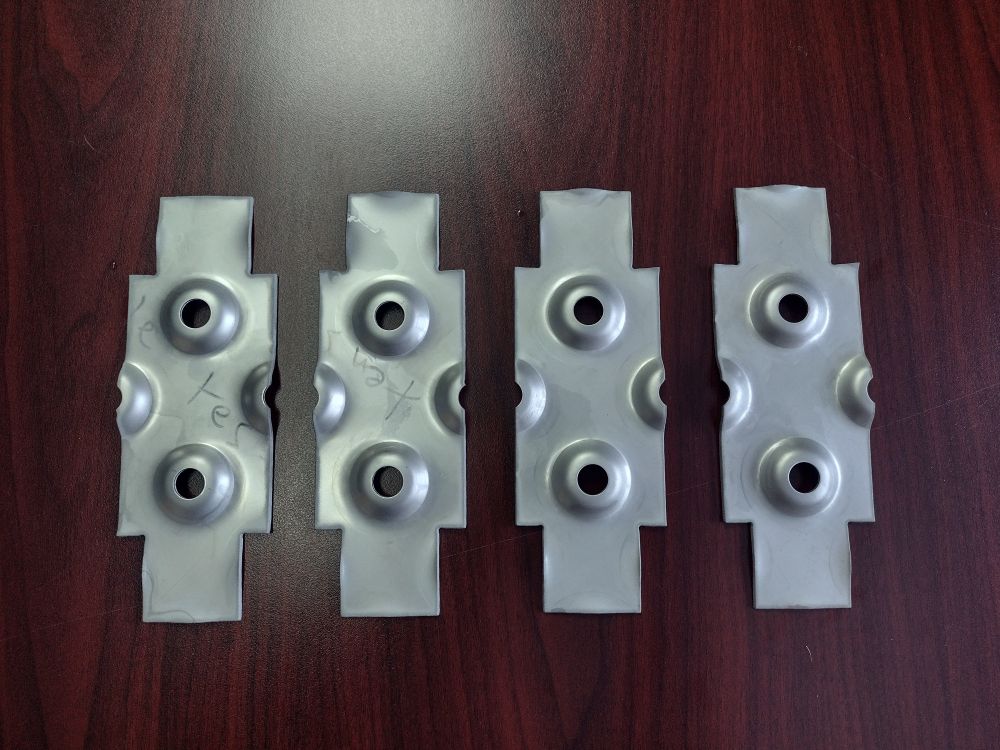 Pieces cut from dimpled sheet metal, laying on a wooden surface.