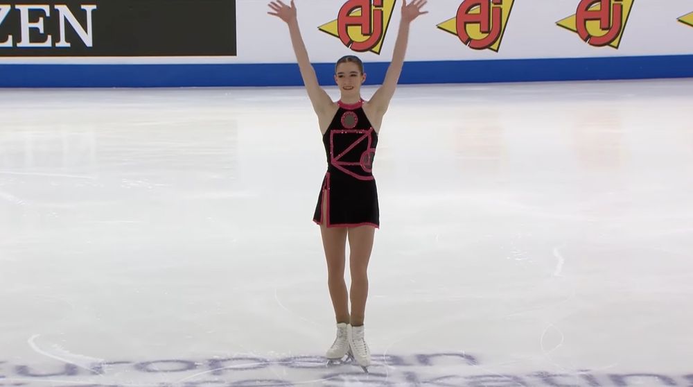 Italian figure skater Lara Naki Gutmann finishes her short program at the European Championships. She has her arms in the air waving to the crowd and wears a black and pink dress with a geometric pattern — a callout to the television series "Squid Game."