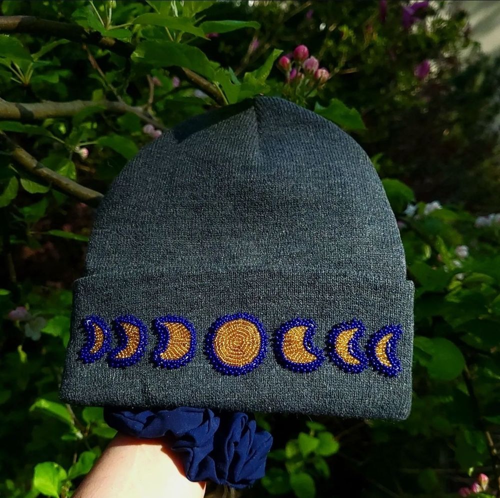 7 moon phases beaded onto a grey beanie. The beads are gold and dark blue 