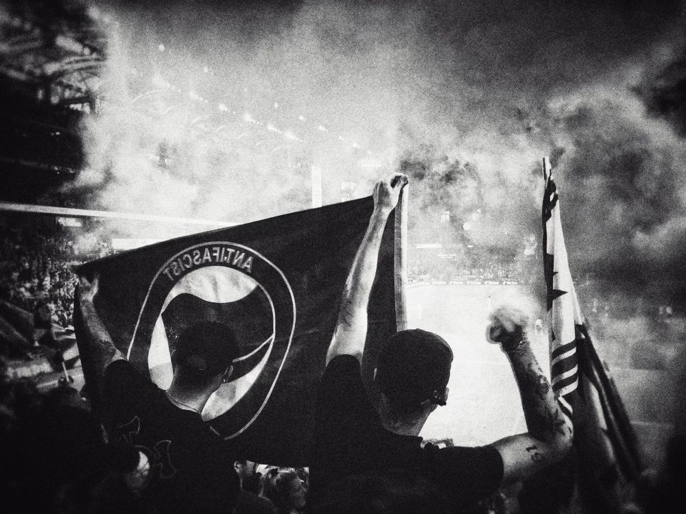 Two PTFC supporters hold an anti-fascist flag in a smoked filled North end of providence park. 