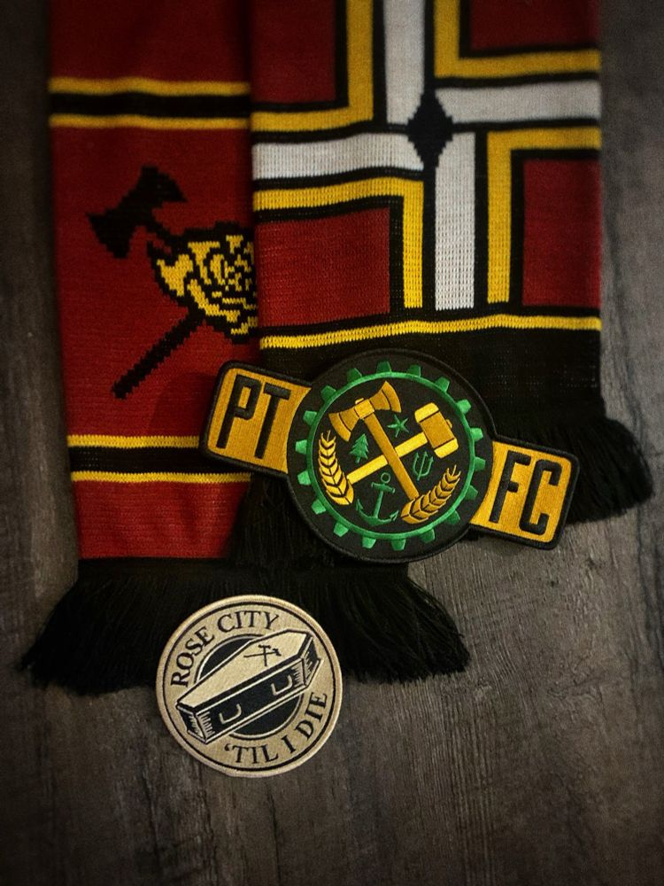 A scarf showing the Portland city flag and the Timbers Army Axe & Rose logo embroidered on it. Two patches: a patch with a coffin and cross axes saying “rose city ‘til I die” and a patch that says “PTFC” with elements from the Portland city crest that include wheat, tree, trident, anchor, star, hammer & axe. 
