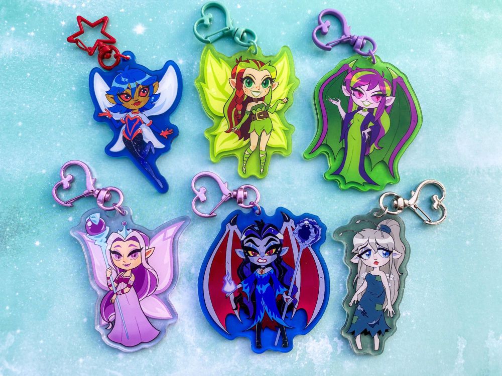 A photo of acrylic charms of the Faeries from Neopets lined up on a teal, cloudy looking background.
The top row is Mira The Space Faerie, Illusen, and Jhudora. The bottom row is Queen Fyora, The Darkest Faerie, and Baelia the grey faerie.