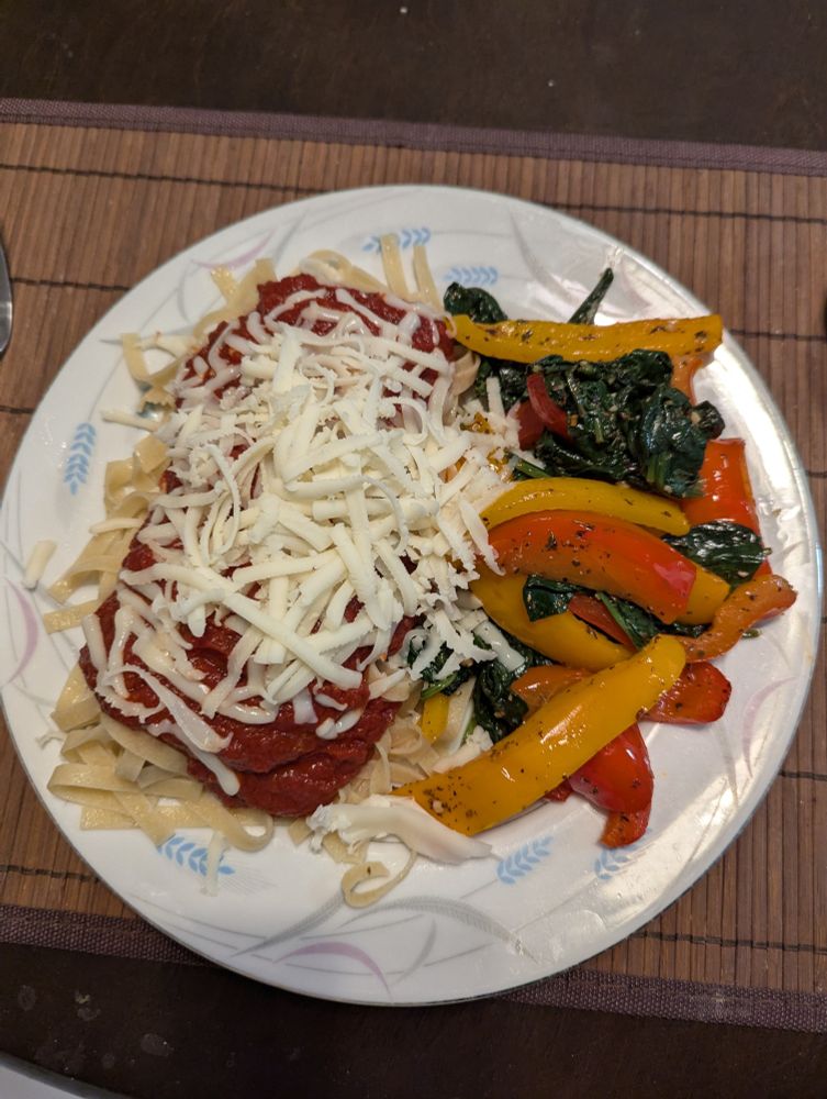 Fettuccine with meatballs in marinara sauce, topped with mozzarella. On the side is sauteed spinach with red and orange bell peppers.